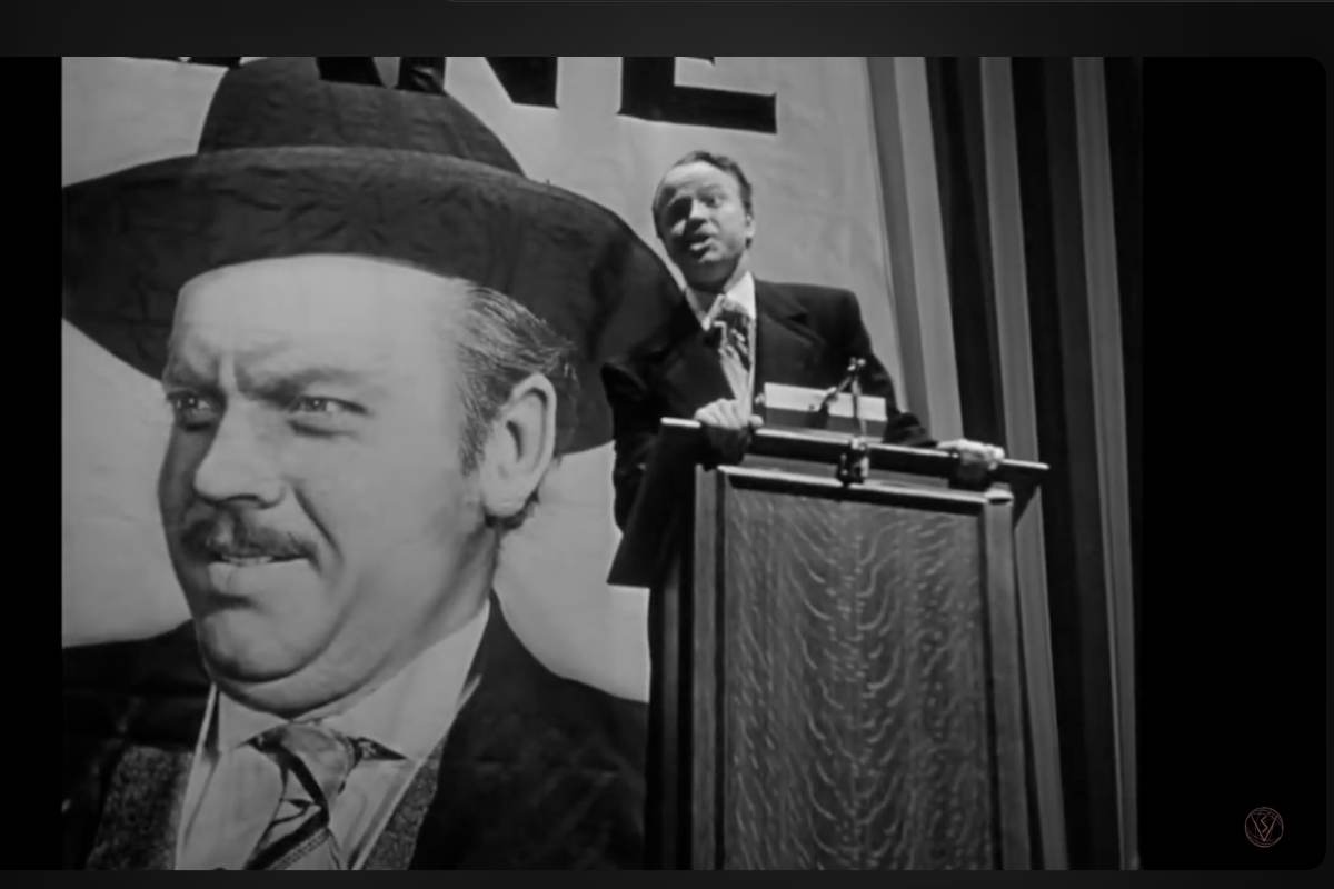 Orson Welles in una scena del film, sullo sfondo la scritta Kane e il poster con il volto di Orson Welles