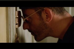 Jean Reno guarda dallo spioncino della porta in una scena del film Léon