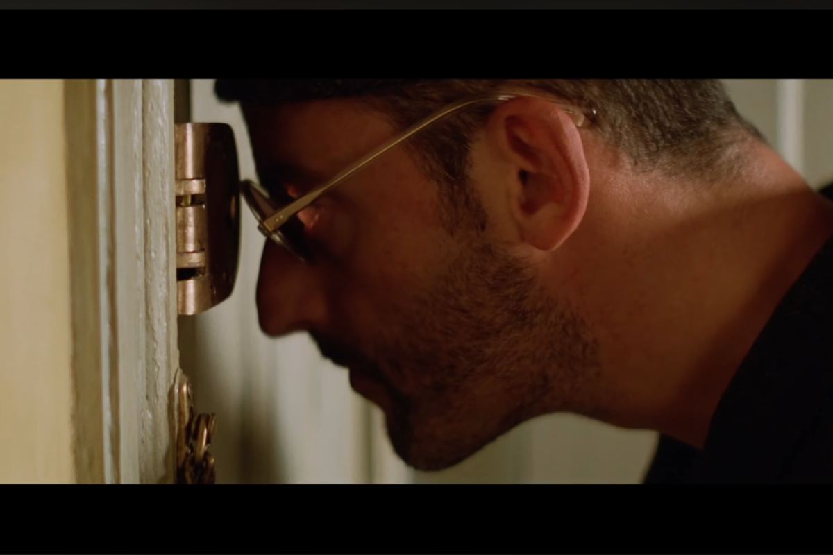 Jean Reno guarda dallo spioncino della porta in una scena del film Léon