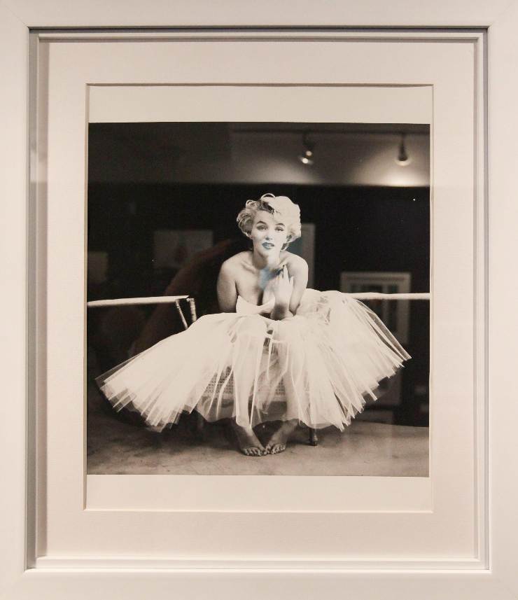 Una foto incorniciata che mostra Marilyn chinata a terra con un abito bianco