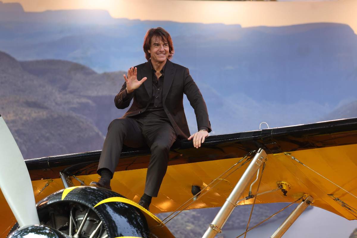 Tom Cruise saluta seduto sull'ala di un aereo