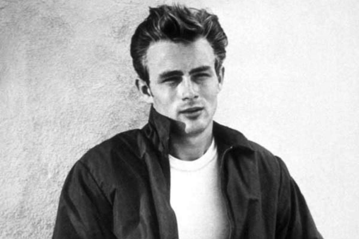 James Dean appoggiato ad una parete con una giacca nera e la maglietta bianca