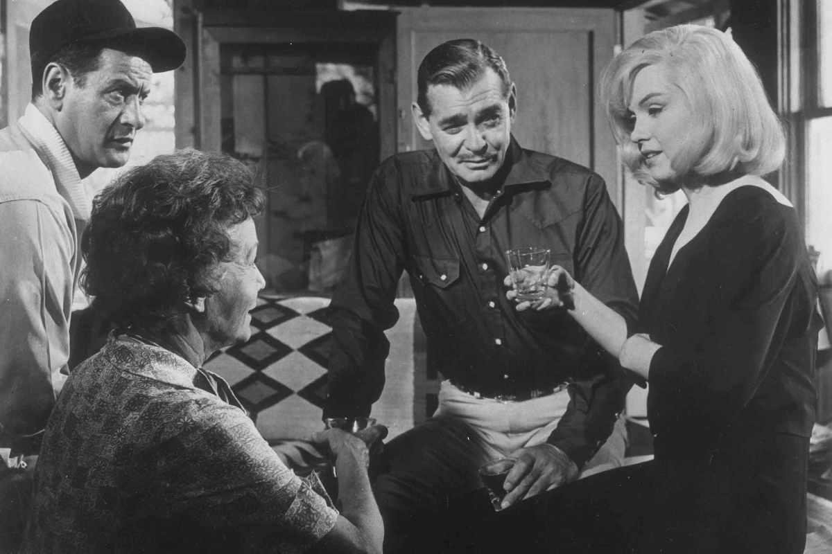 Marilyn Monroe un bicchiere in mano mentre chiacchiera, accanto a lei Clark Gable