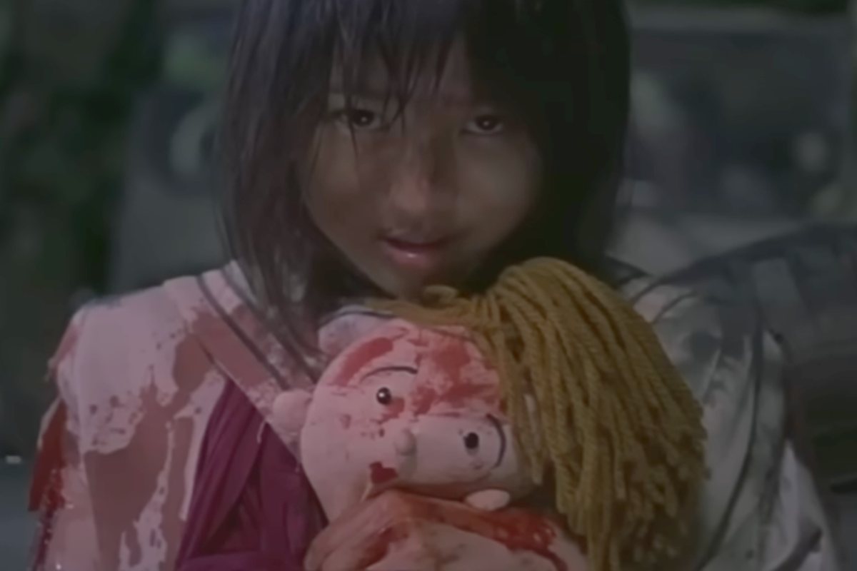 Una ragazza insanguinata guarda fisso nell'obiettivo con in mano un peluche, è una scena del film Battle Royale 