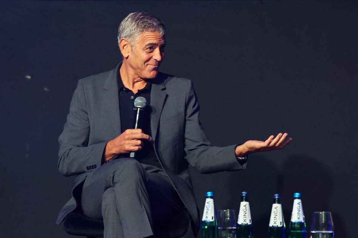 George Clooney seduto con il microfono in mano durante una conferenza