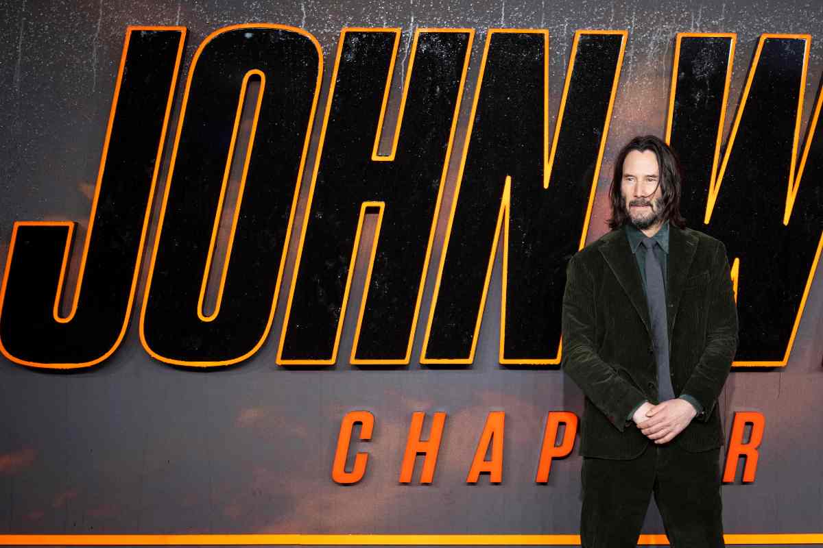 Keanu Reeves in piedi con dietro il poster di John Wick alla prima 