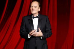 Quentin Tarantino in smoking con sullo sfondo una tenda da teatro rossa