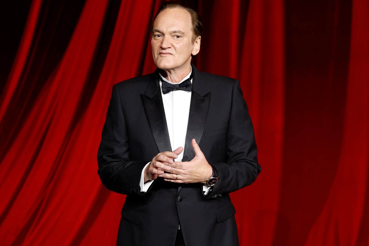 Quentin Tarantino in smoking con sullo sfondo una tenda da teatro rossa
