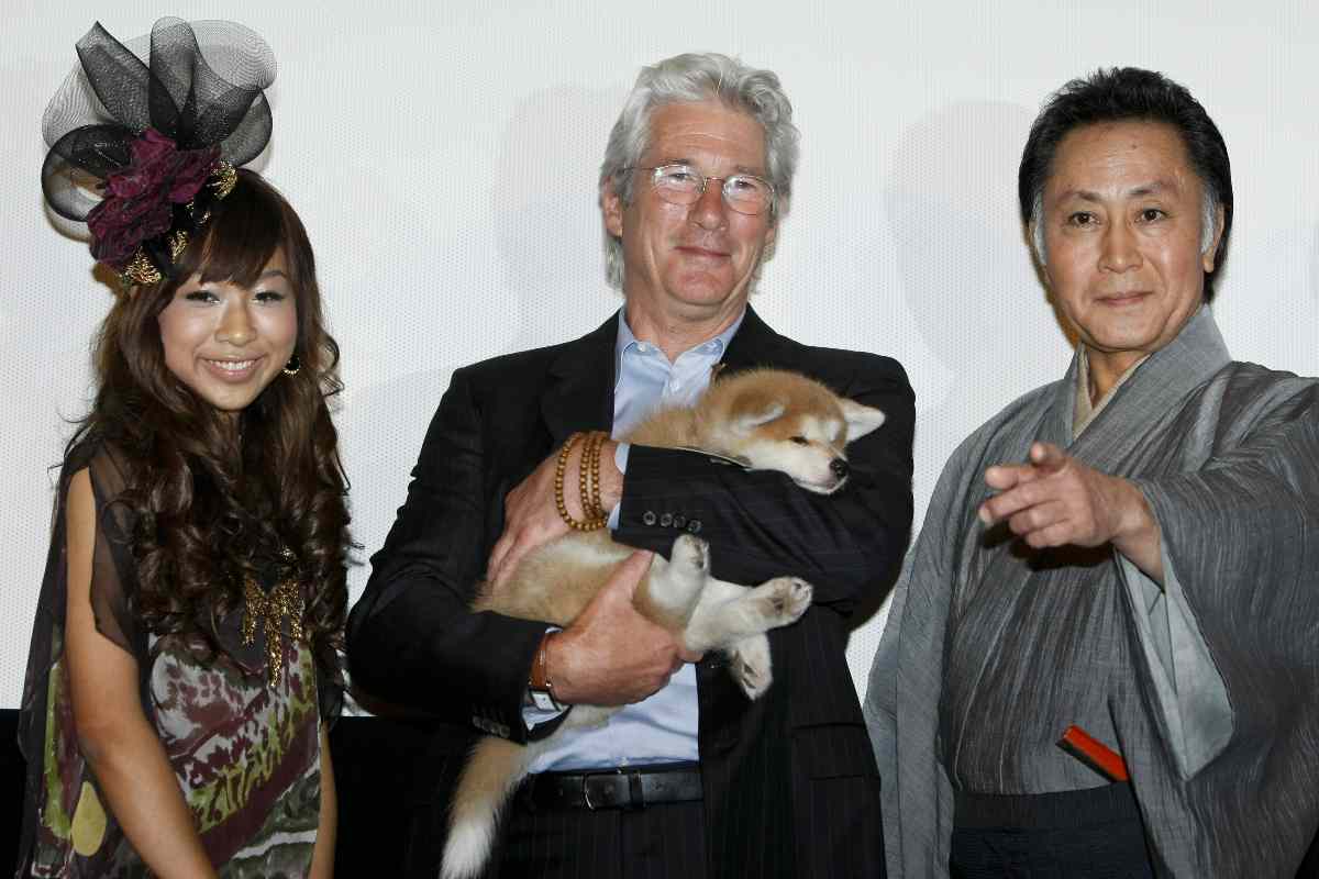 Richard Gere con in braccio un cucciolo di Akita Inu e due persone accanto a lui
