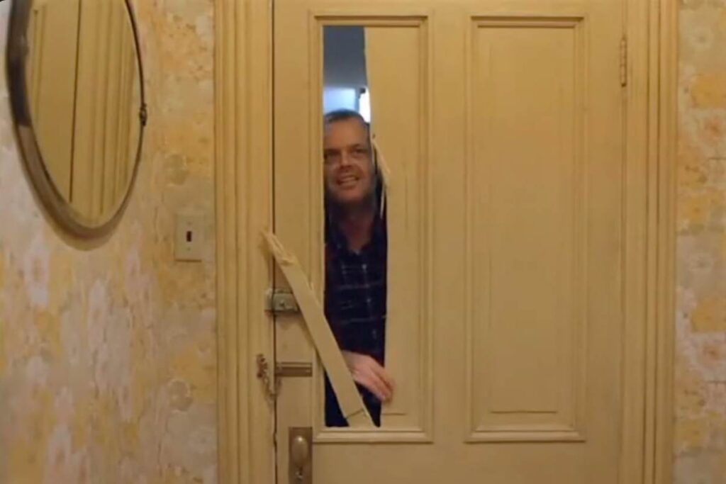 Jack Nicholson in Shining dietro alla porta rotta dall'ascia