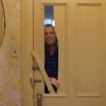 Jack Nicholson in Shining dietro alla porta rotta dall'ascia