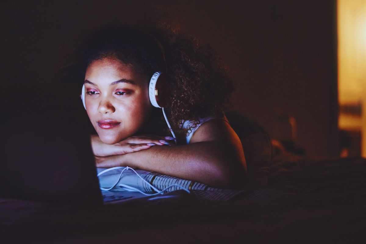 Ragazza distesa sul letto che guarda un film indossando le cuffie