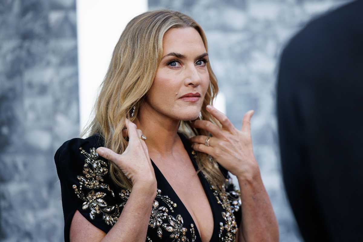 Kate Winslet con i capelli sciolti se li tocca per spingerli indietro è di profilo e ha lo sguardo rivolto altrove