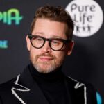 Macaulay Culkin primo piano con un abito elegante e un paio di occhiali dalla montatura nera, posa per i fotografi