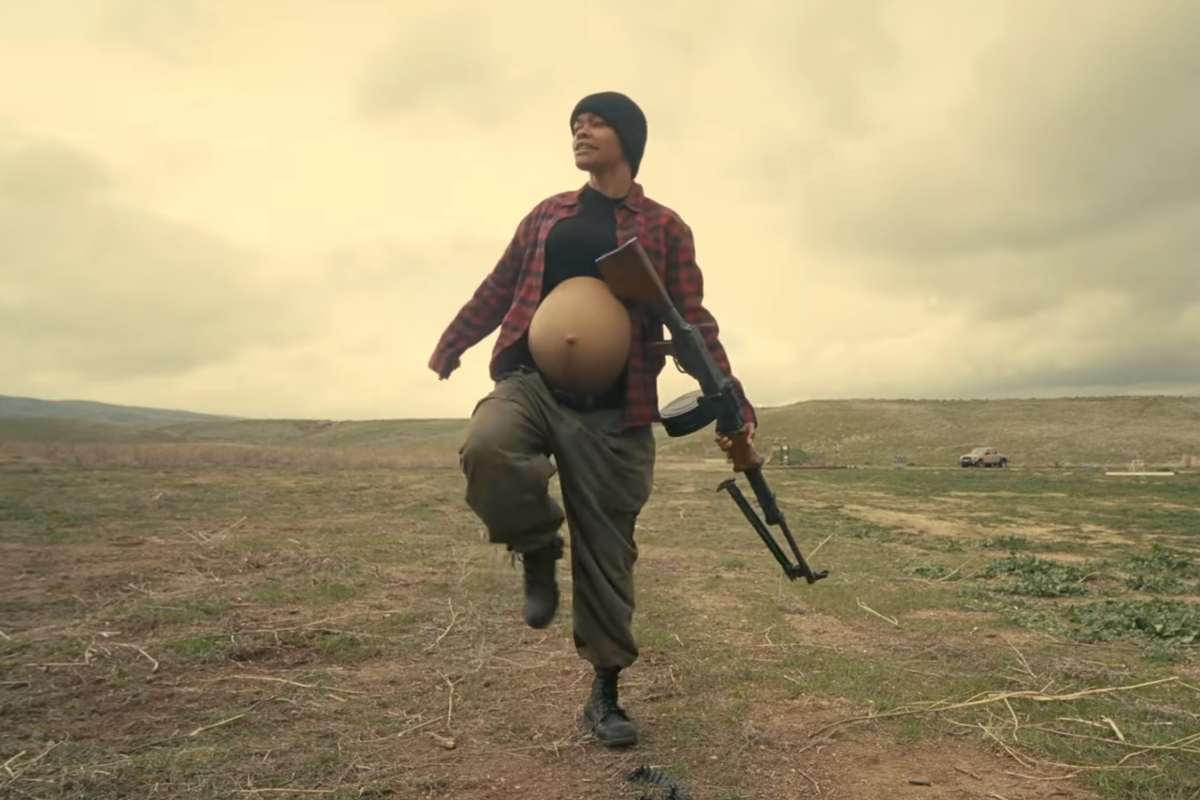 Tayana Taylor in una scena del film è incinta, con la pancia visibile, una gamba sollevata e un mitra in mano