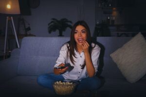 Ragazza che mangia popcorn su divano mentre guarda la televisione