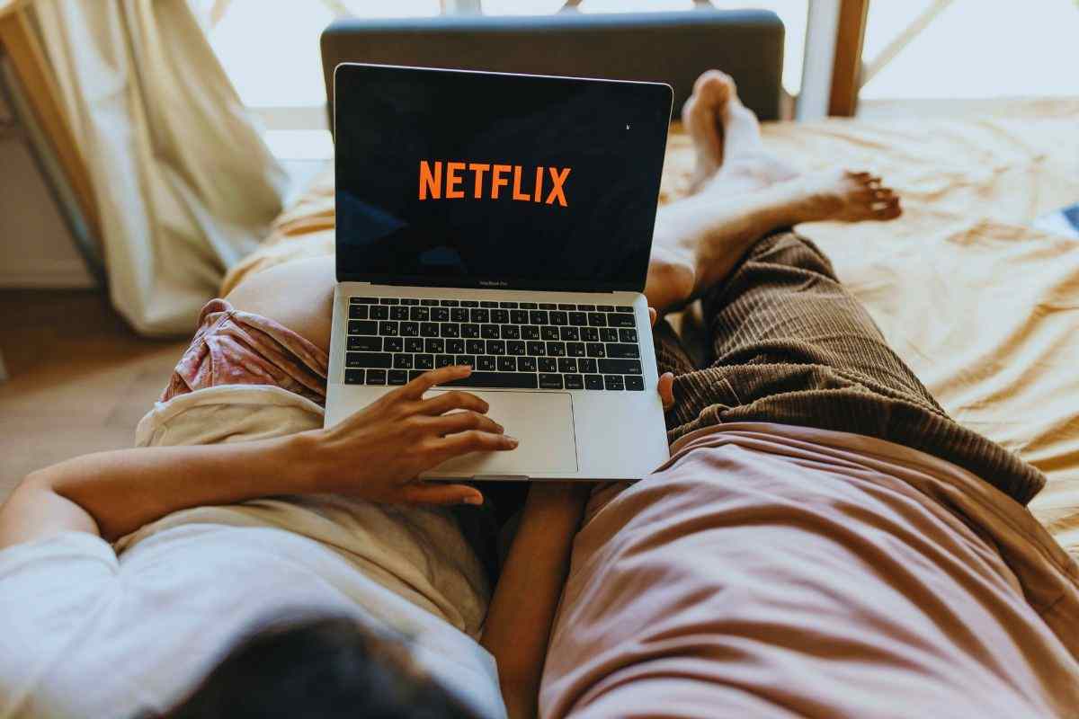 Copia distesa a letto che guarda Netflix dal PC portatile