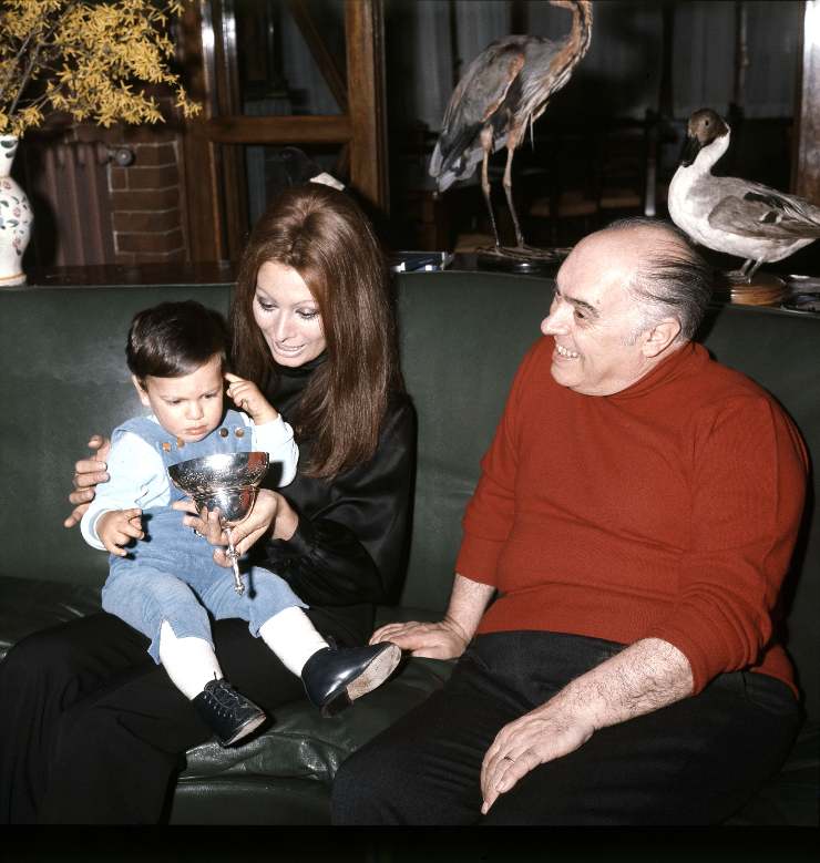 Sophia Loren seduta su un divano con in braccio il figlio Carlo Ponti Jr e accanto il marito Carlo Ponti