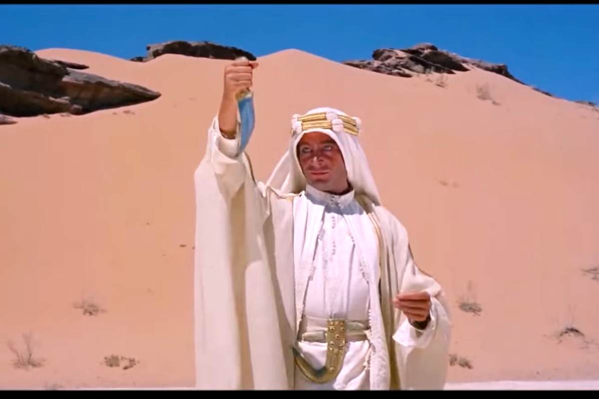 Peter O'Toole in una scena del film 'Lawrence d'Arabia' vestito da arabo tutto in bianco solleva un pugnale e si guarda riflesso