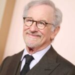 Steven Spielberg in posa vestito elegante accenna un sorriso