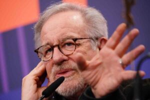 Steven Spielberg al microfono parla ai giornalisti con la mano sinistra sollevata