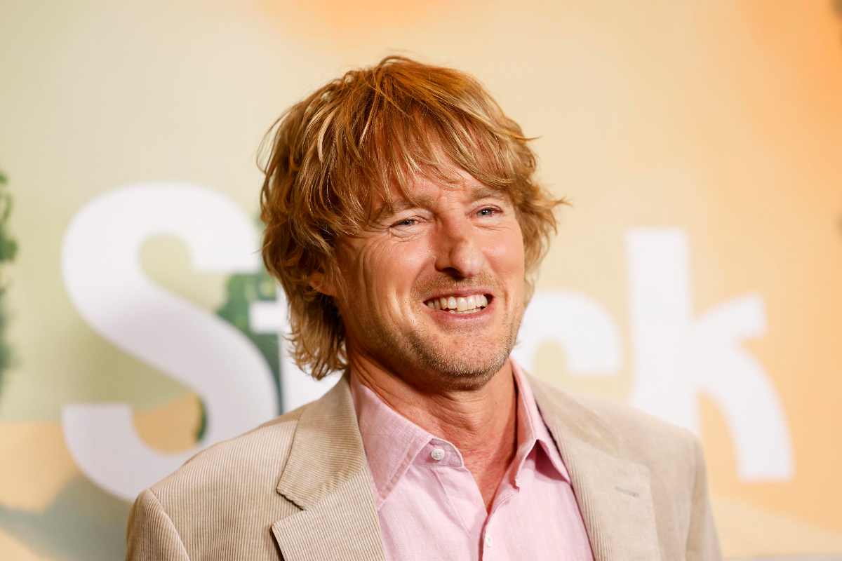 Owen Wilson sorride in posa in abito marrone con camicia rosa