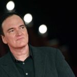 Quentin Tarantino in giacca e camicia nera sullo sfondo tre luci