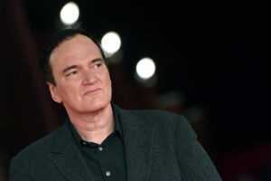 Quentin Tarantino in giacca e camicia nera sullo sfondo tre luci