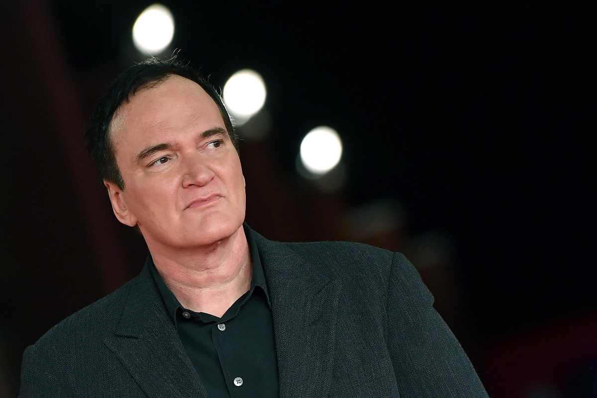 Quentin Tarantino in giacca e camicia nera sullo sfondo tre luci