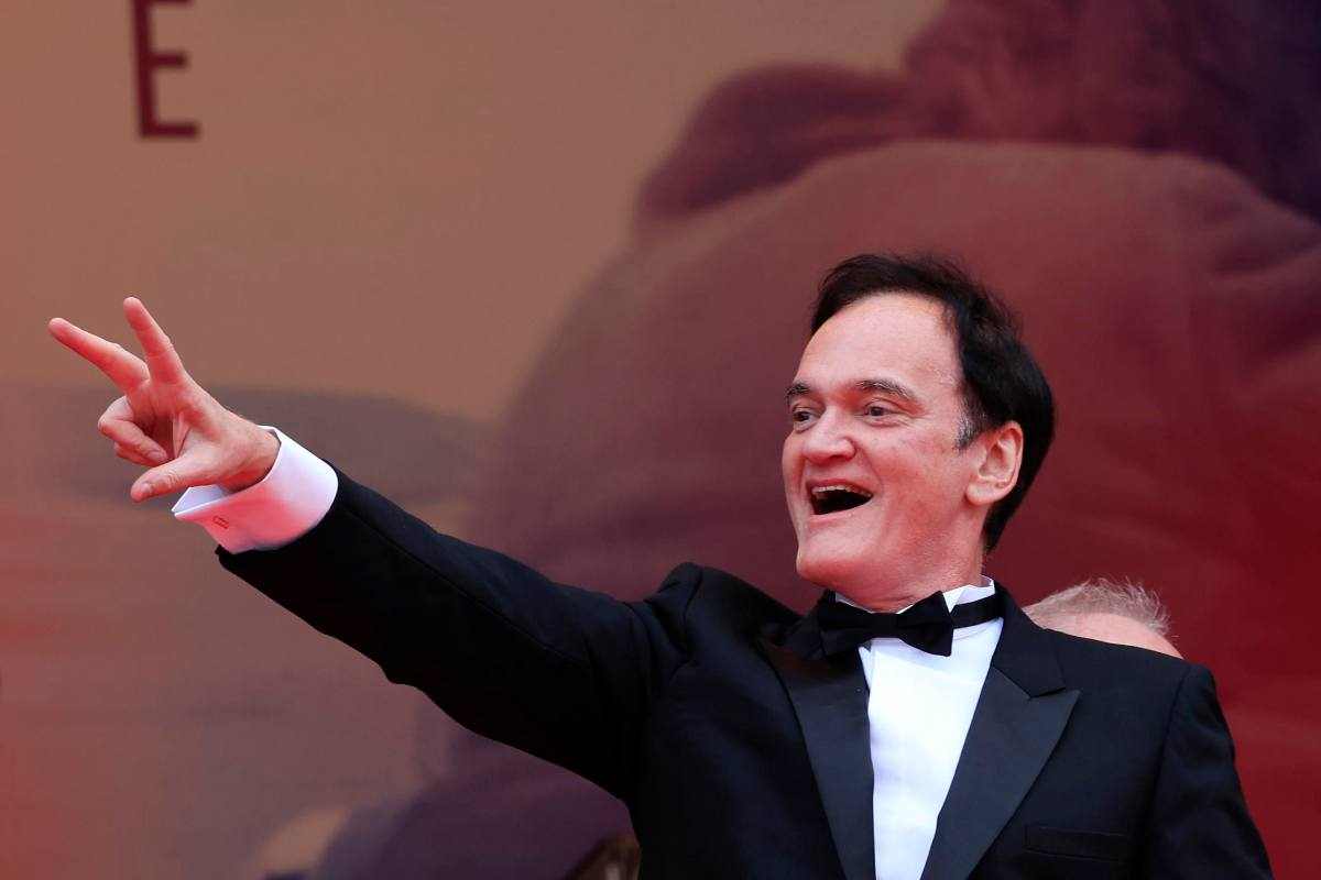 Quentin Tarantino in smoking alza il braccio destro e fa un gesto