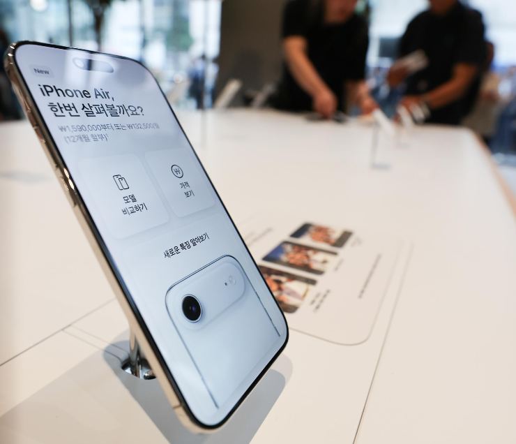 Un iPhone 17 appoggiato ad un supporto e collocato su un tavolo di legno bianco in quello che sembra essere un negozio Apple Store