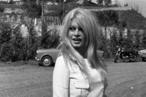 Brigitte Bardot con un abito bianco alle sue spalle una macchina