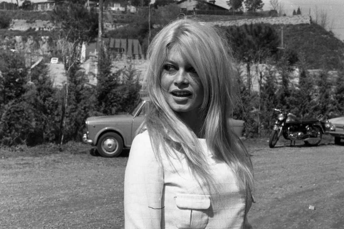 Brigitte Bardot con un abito bianco alle sue spalle una macchina