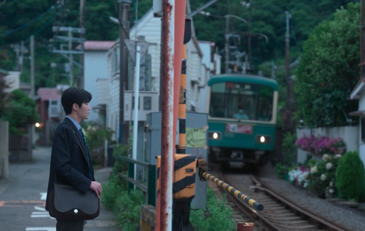 Un giovane uomo attende di fronte ad un passaggio a livello l'arrivo di un treno