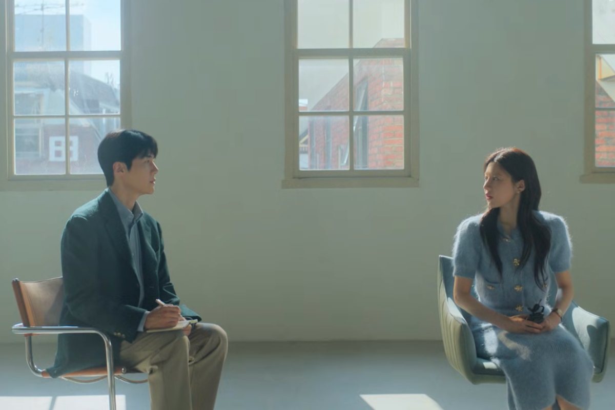 Un uomo e una donna asiatici seduti su due sedie. Sullo sfondo un muro bianco con due finestre