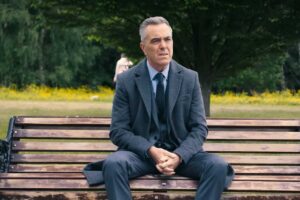 James Nesbitt seduto su una panchina in giacca e cravatta