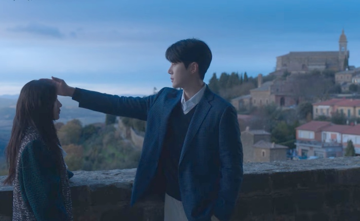 Due asiatici, sullo sfondo l'Italia. Lui solleva la mano e la pone sul capo di lei.