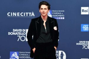 Timothée Chalamet in posa per i fotografi, indossa un abito nero e ha le mani in tasca