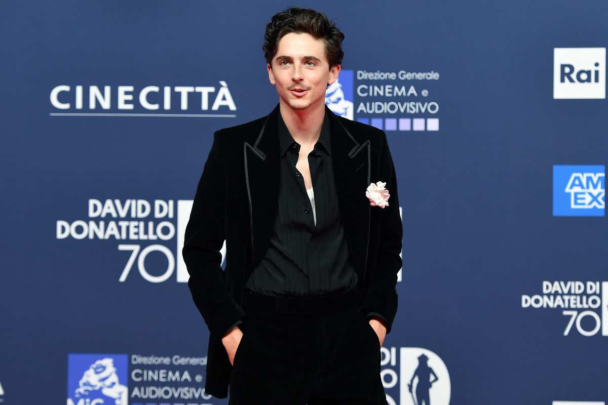 Timothée Chalamet in posa per i fotografi, indossa un abito nero e ha le mani in tasca