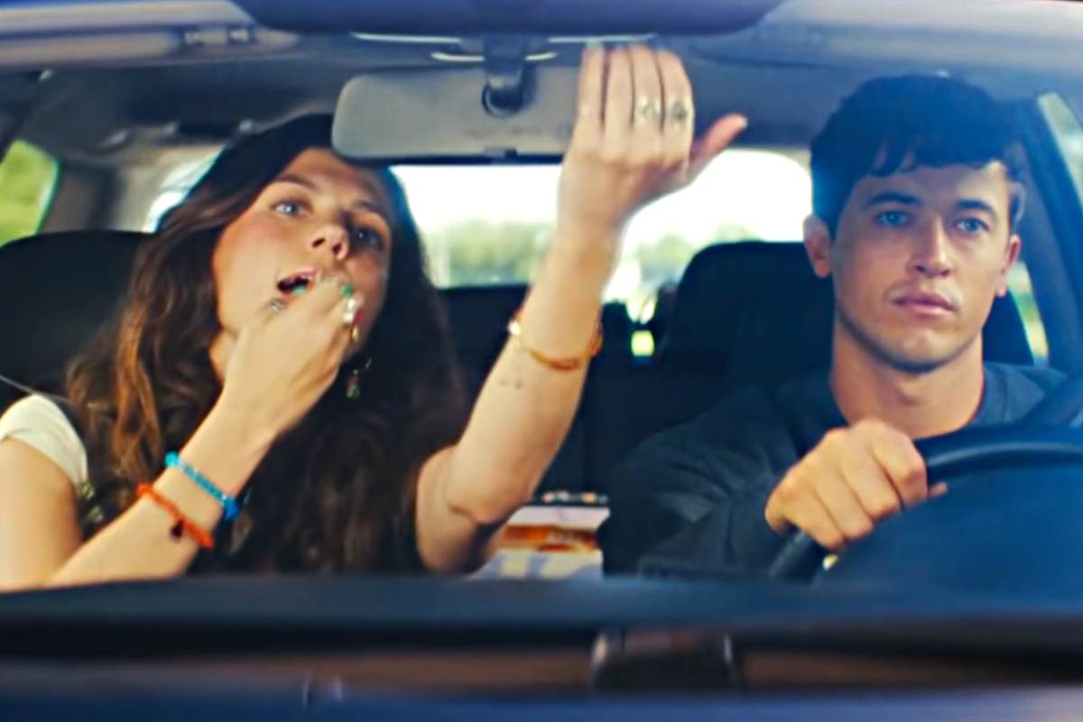 Un uomo e una donna in auto, lei si trucca guardandosi allo specchietto retrovisore 