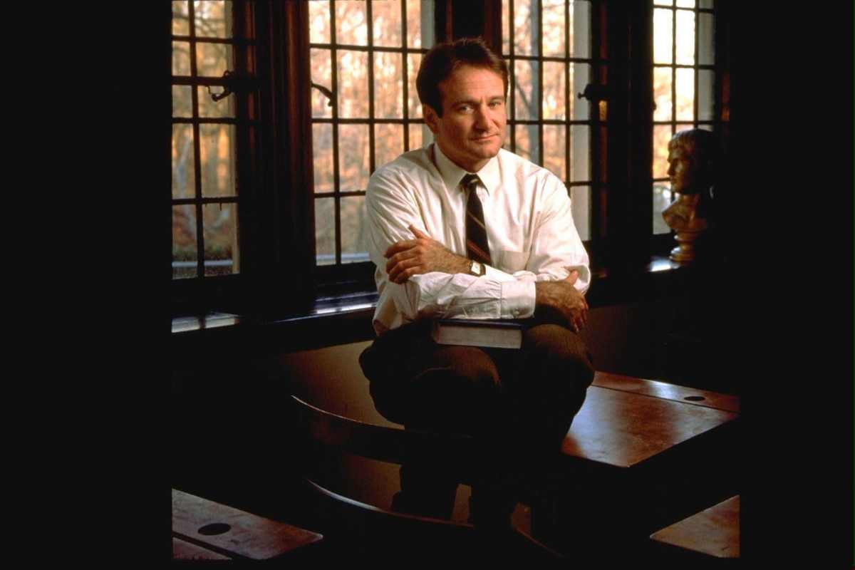 Robin Williams appoggiato ad una cattedra a braccia conserte in una scena del film 'L'attimo fuggente'