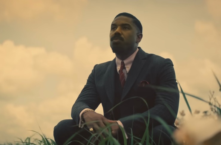 Michael B Jordan accovacciato a terra in mezzo all'erba in una scena di Sinners