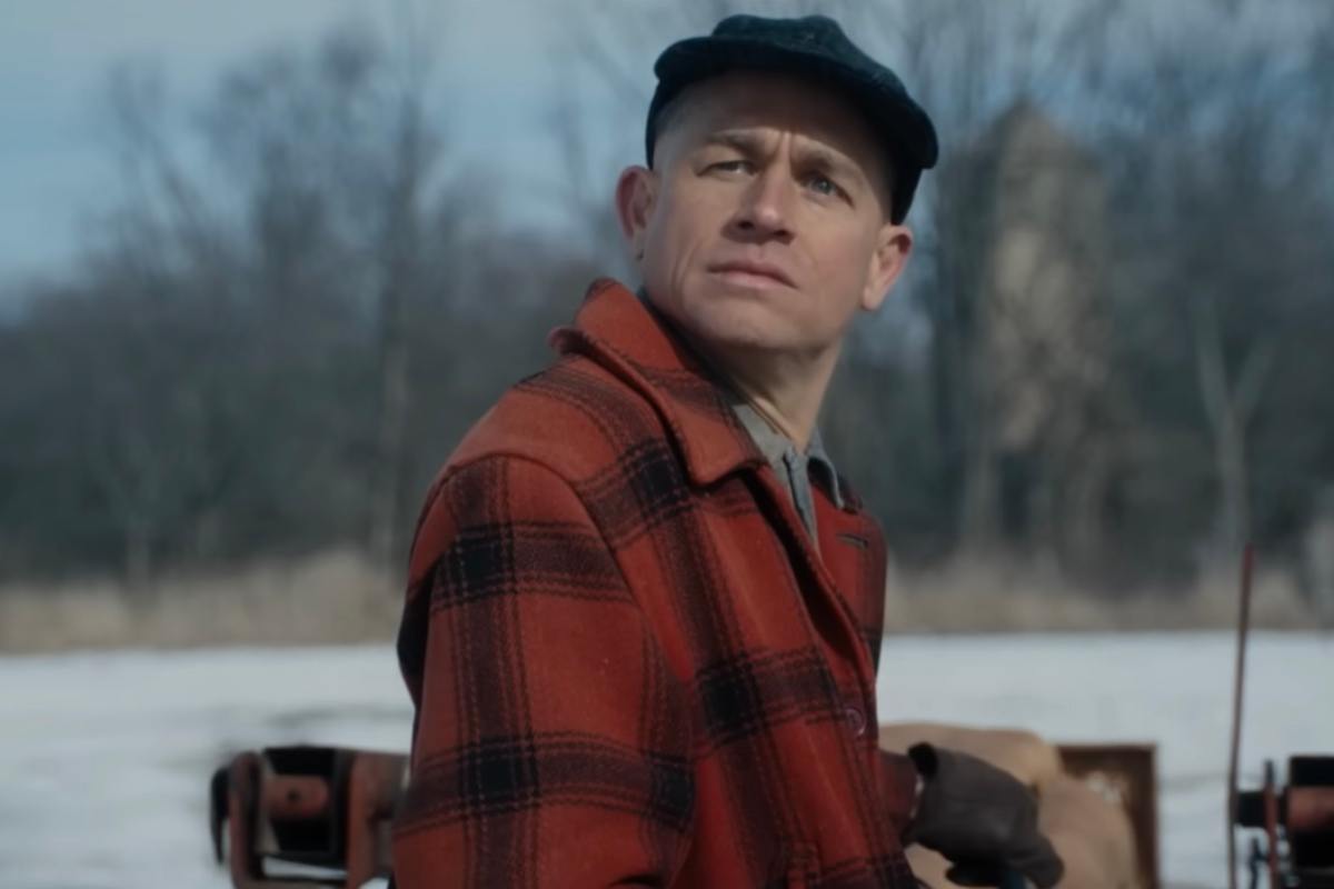 Charlie Hunnam nei panni del killer Ed Gein in una scena di Monster con una giacca scozzese rossa e nera e un berretto tipo coppola in testa