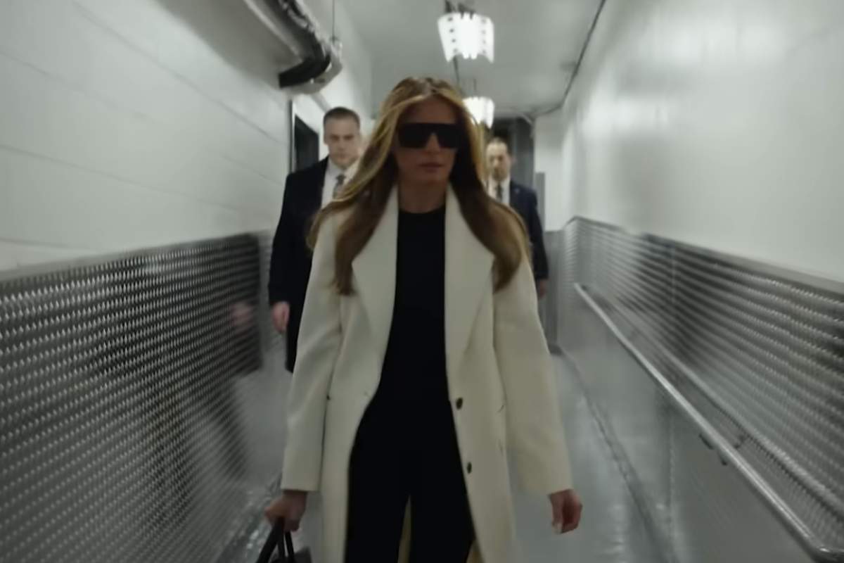 Melania Trump con indosso un cappotto bianco cammina lungo un corridoio 