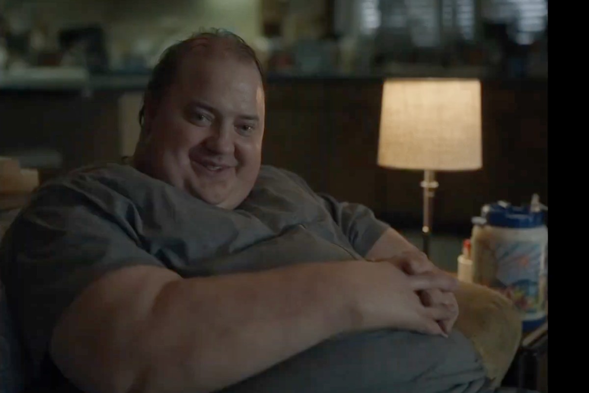 Brendan Fraser nel ruolo di Charlie in The Whale ingrassato seduto su una poltrona sorride