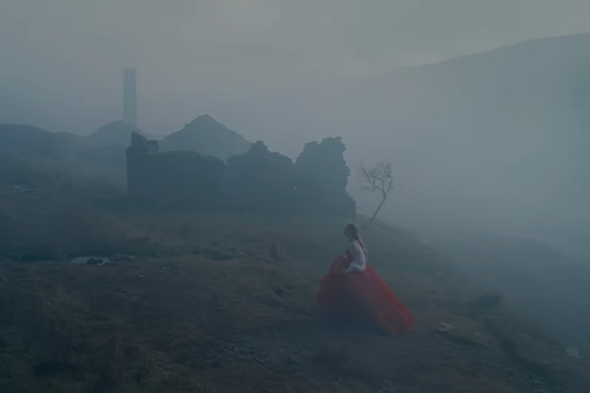 Margot Robbie nella nebbia corre tra le rovine di un villaggio di pietra in Cime Tempestose