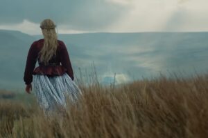 Margot Robbie di spalle cammina nella brughiera in Cime Tempestose