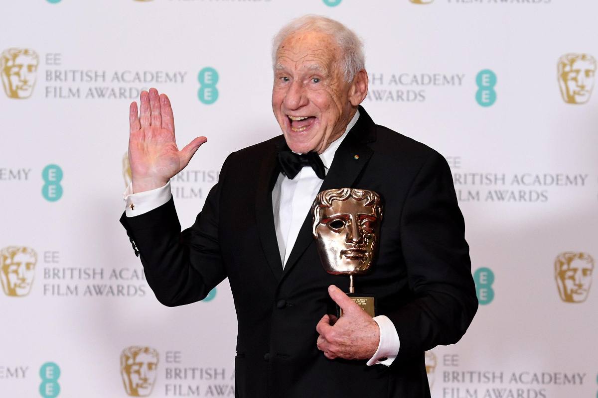 Mel Brooks saluta con la mano mentre stringe in mano un premio