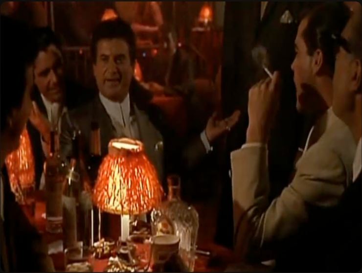 Joe Pesci seduto in un locale in mezzo ad altre persone in una scena del film 'Quei bravi ragazzi'
