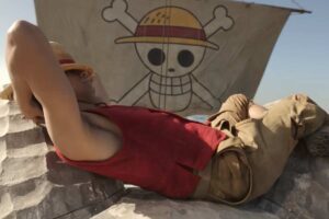 Il personaggio di One Piece Monkey D. Rufy sdraiato su un lato con alle spalle la bandiera dei pirati suo simbolo con un teschio ed un cappello in testa